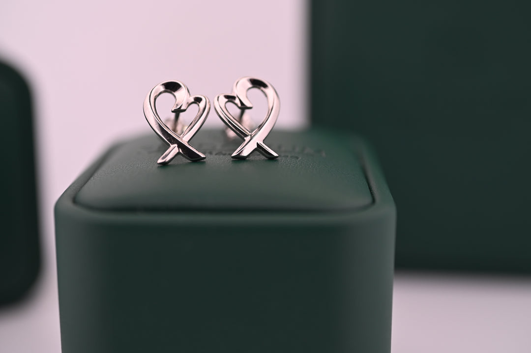 Cercei din platină Eros eleganți și rafinați, simbolizând iubirea, ideali pentru cadou, pe un suport verde elegant.