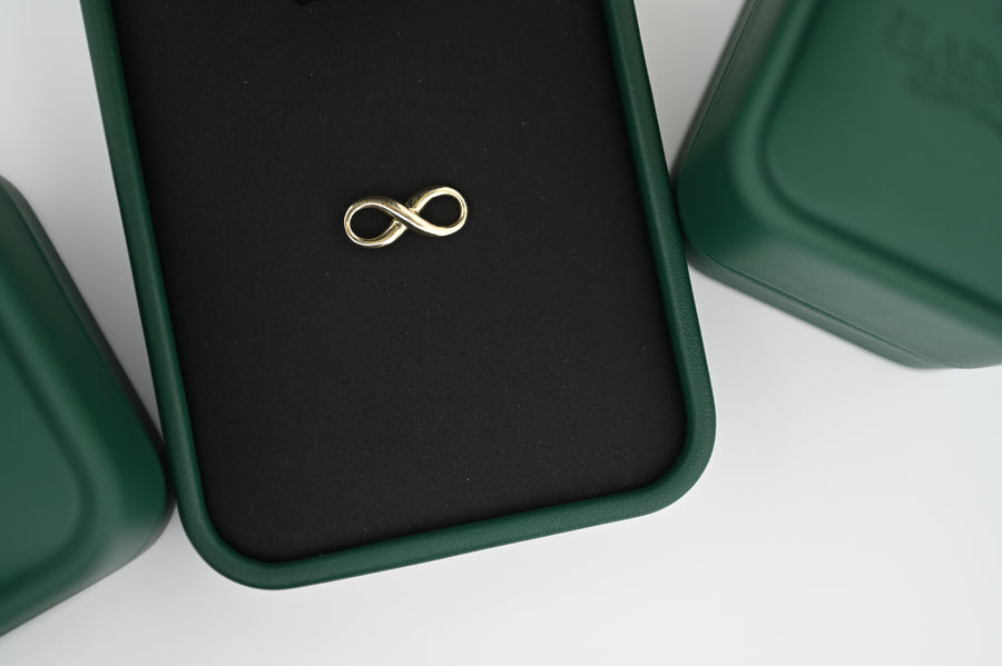 Pandantiv Aur Artemis elegant în formă de infinit, așezat într-o cutie verde, simbolizând eleganța și perfecțiunea atemporală.