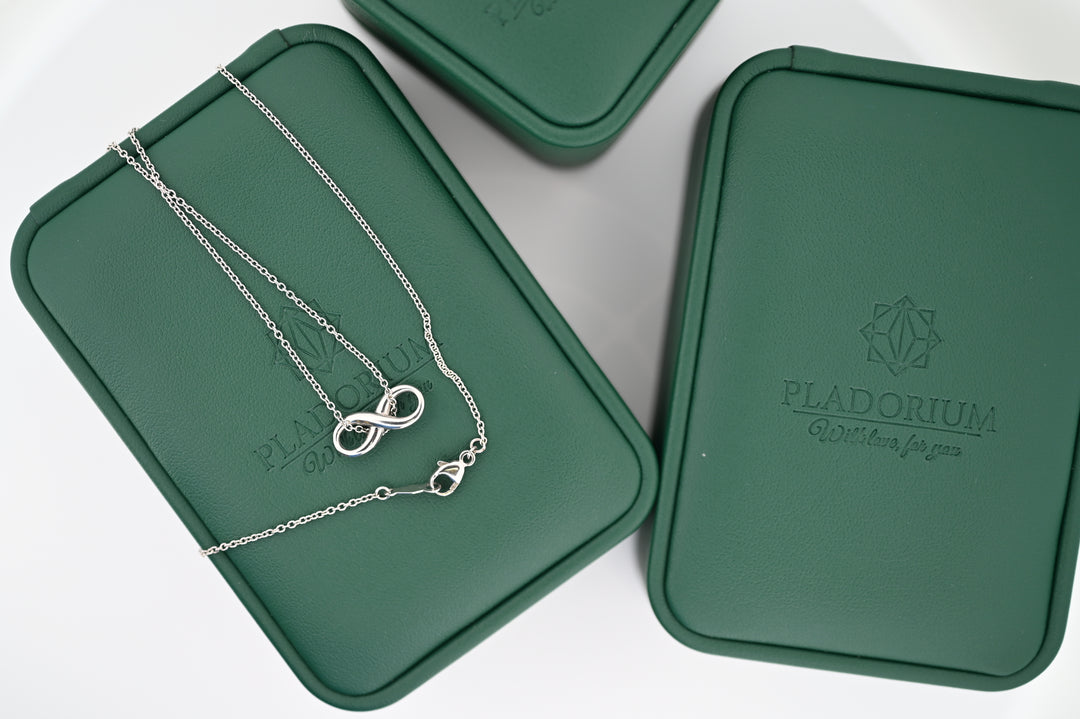 Elegant necklace with infinity pendant on green Pladorium boxes, symbolizing luxury and timeless style for women.