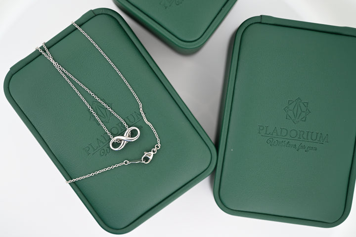 Elegant necklace with infinity pendant on green Pladorium boxes, symbolizing luxury and timeless style for women.