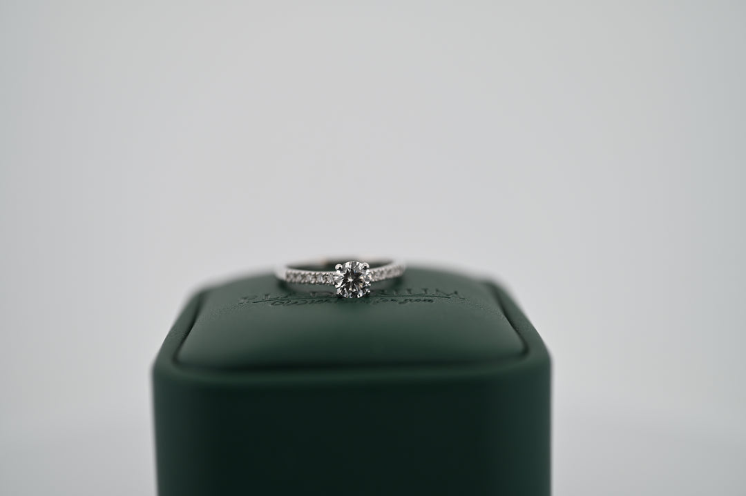 Elegant inel de logodnă din aur sau platină cu diamant natural central de 0.5 ct și 10 diamante decorative, pe un suport verde.