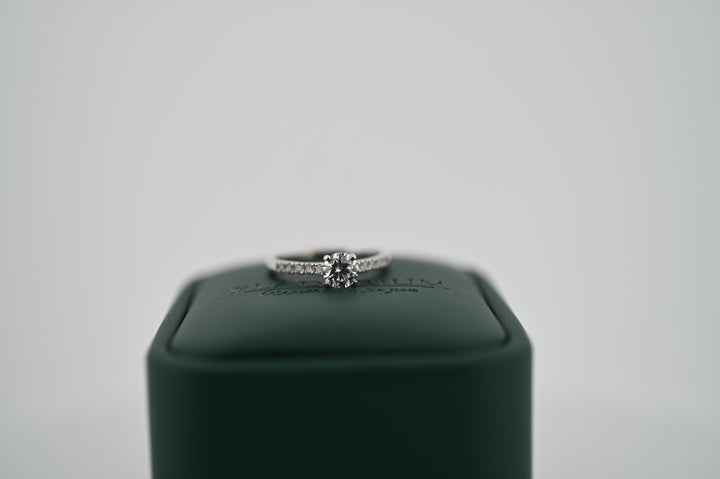 Elegant inel de logodnă din aur sau platină cu diamant natural central de 0.5 ct și 10 diamante decorative, pe un suport verde.